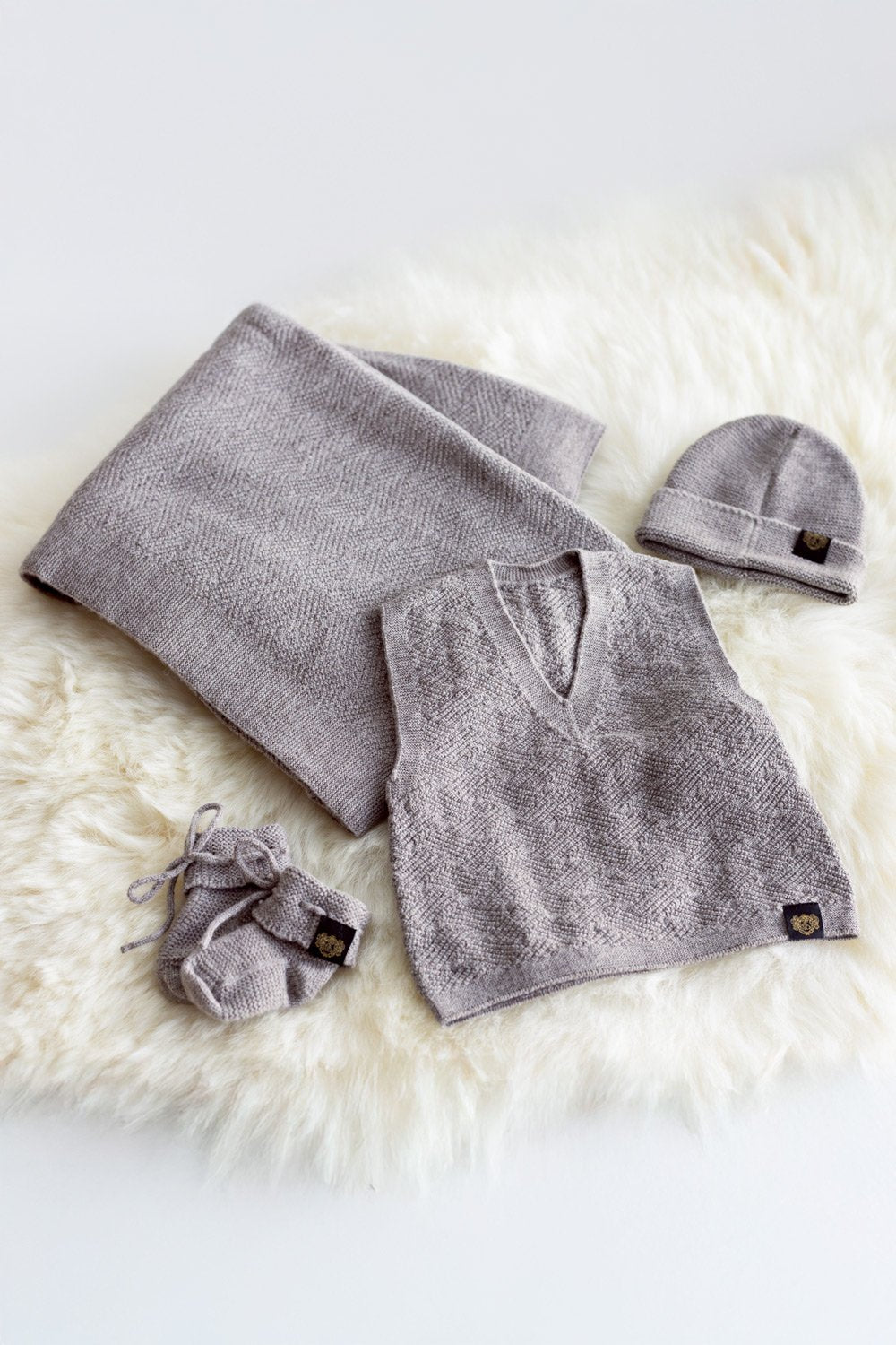 Newborn Pēpē Merino Gift Set by McDonald with blanket, hat, and booties on a white fur surface