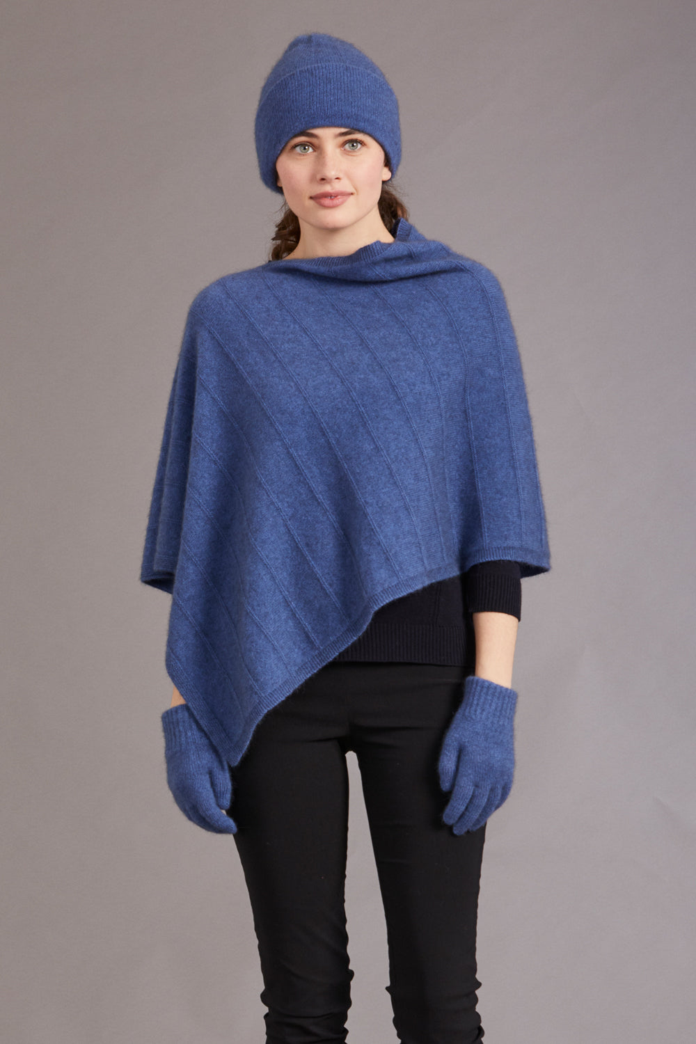 Woman wearing a blue poncho, beanie, and gloves on a gray background