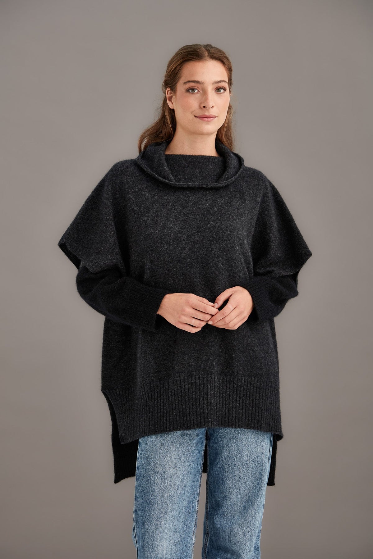 Woman wearing the Step Hem Possum Merino Poncho in Charcoal by McDonald against a plain background - front view