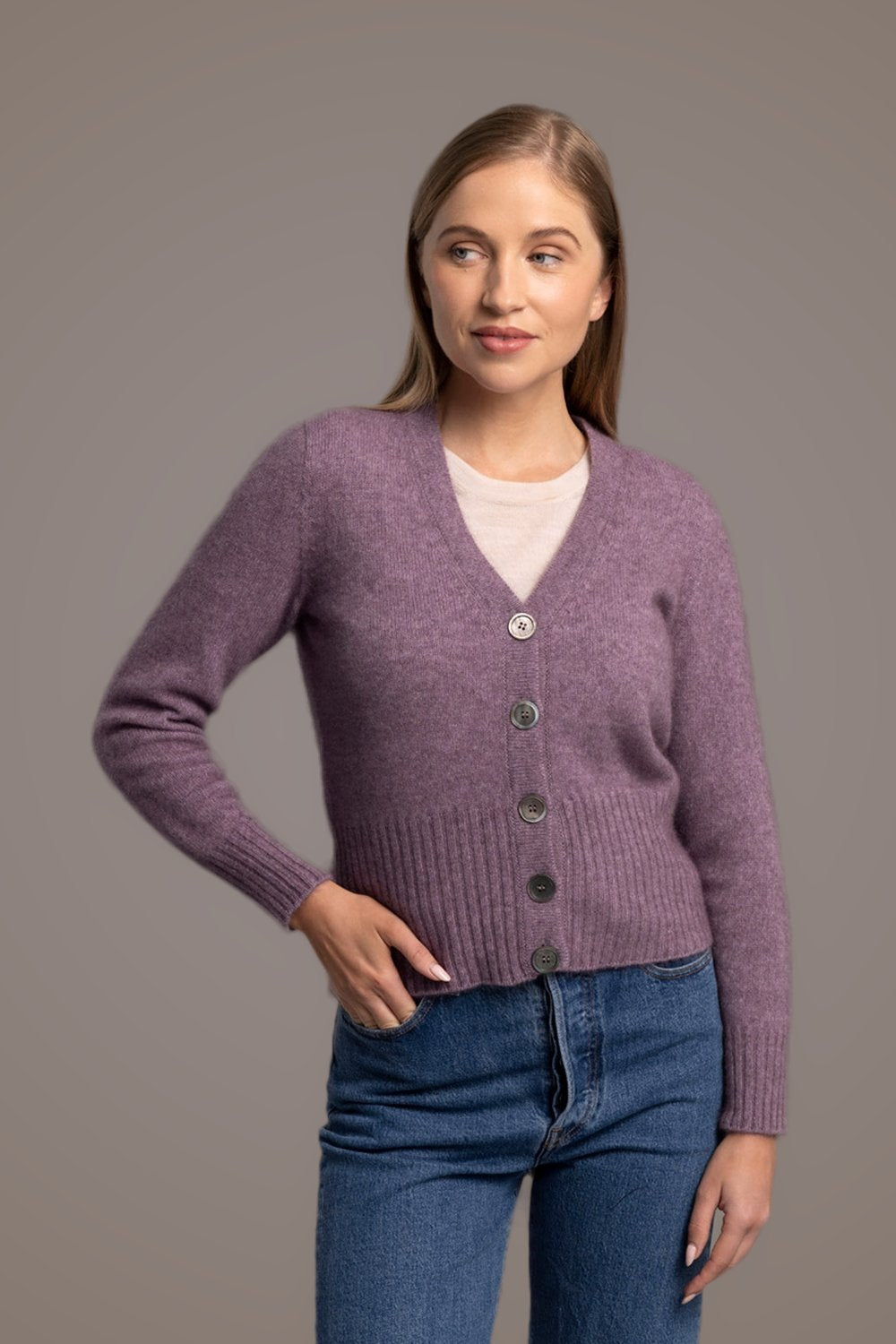 Woman wearing the Rib Possum Merino Cardi in Lilac by McDonald over a white shirt with blue jeans on a gray background