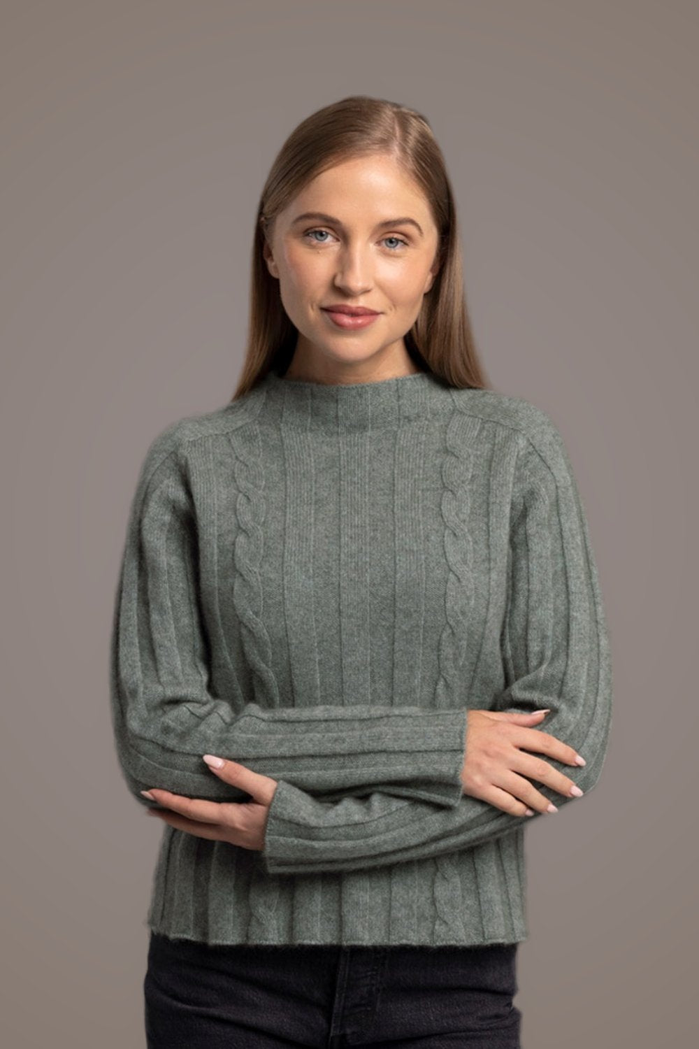 Woman wearing the Corrugated Cable Possum Merino Pullover in Mint by McDonald and dark jeans standing against a gray background
