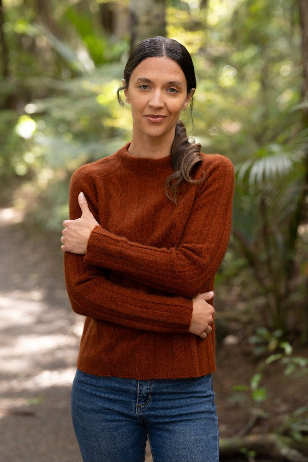 Woman wearing the Corrugated Cable Possum Merino Pullover in Spice by McDonald and blue jeans standing in a forest