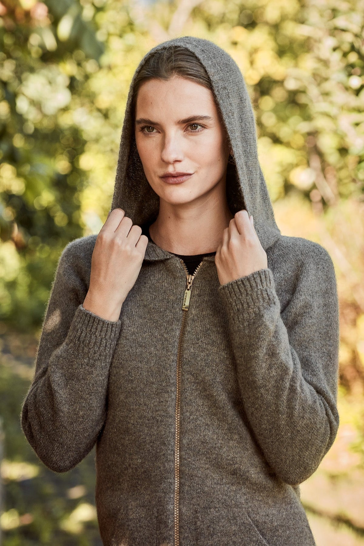 Woman wearing the Stepped Stitch Possum Merino Hoodie in Bark by McDonald New Zealand in a garden setting, alternate view