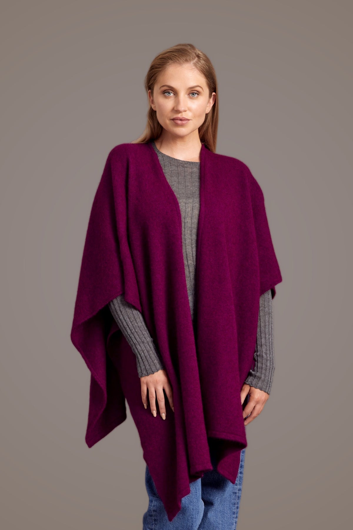 Woman wearing the Split Front Possum Merino Wrap in Berry by McDonald over a gray sweater and blue jeans on a brown background