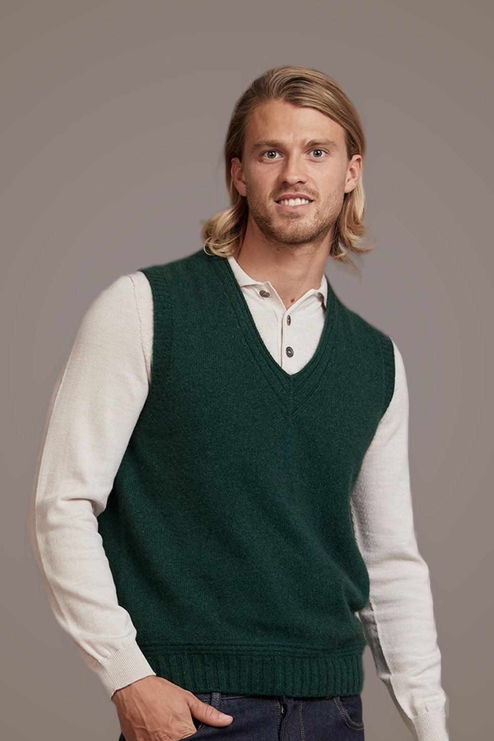 Man smiling wearing the Ridge Possum Merino Vest in Forest by McDonald over a white shirt on a gray background