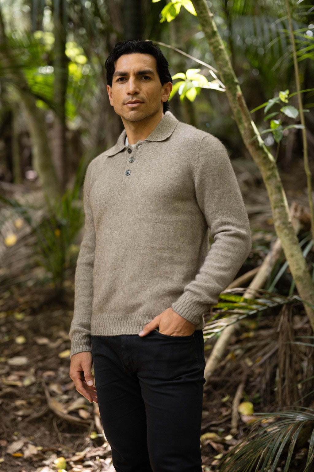 Man standing in a forested area wearing the Stepped Stitch Possum Merino Polo in Mocha by McDonald