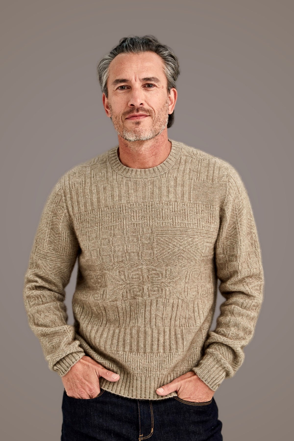 Man wearing the Patchwork Possum Merino Sweater in Mocha by McDonald, with dark jeans against a plain background