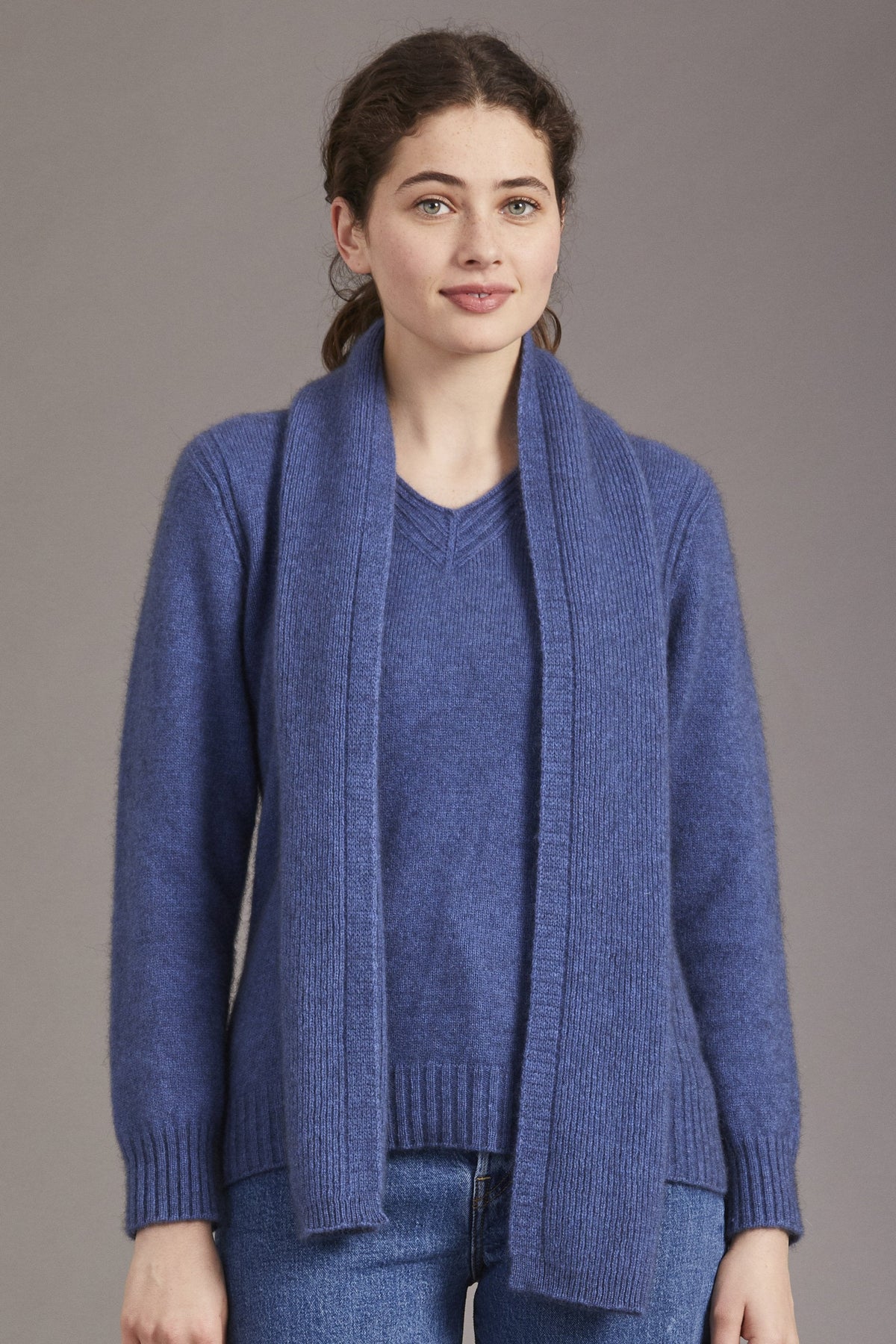 Woman wearing the Fine Rib Possum Merino Scarf in Orchid by McDonald over a matching sweater against a plain background