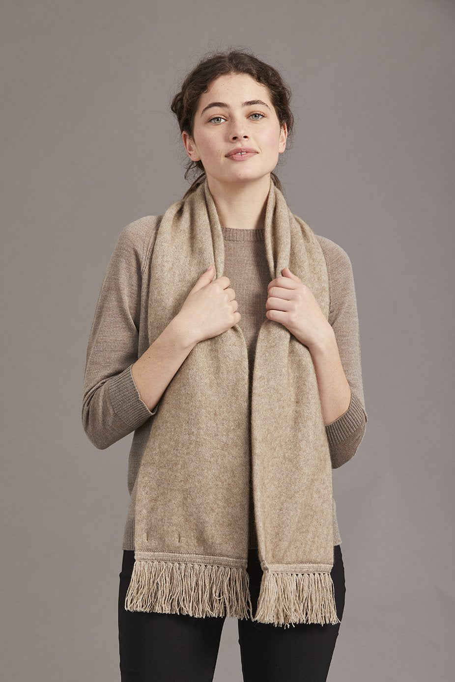Woman wearing the Classic Fringed Possum Merino Scarf in Mocha by McDonald details on a gray background