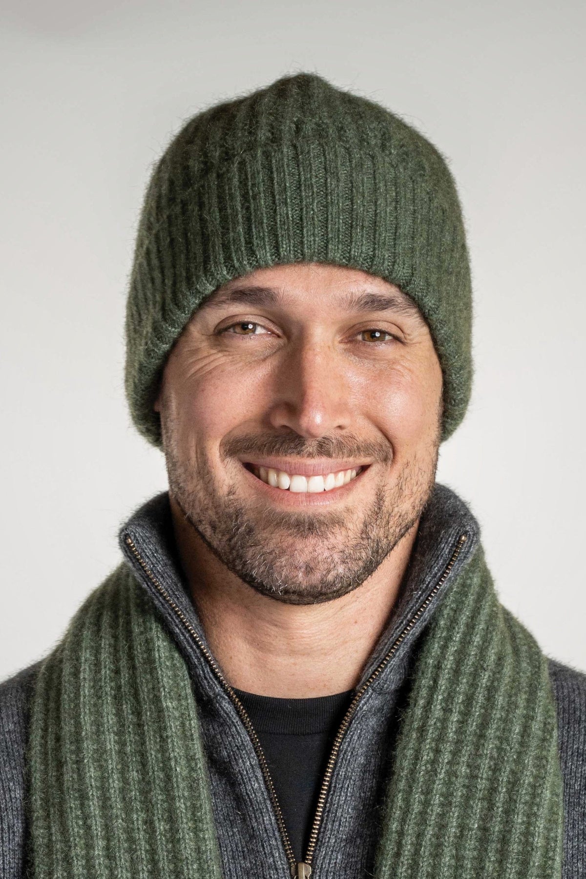 Man wearing the Ribbed Possum Merino Beanie in Moss by Koru with matching scarf against a white background