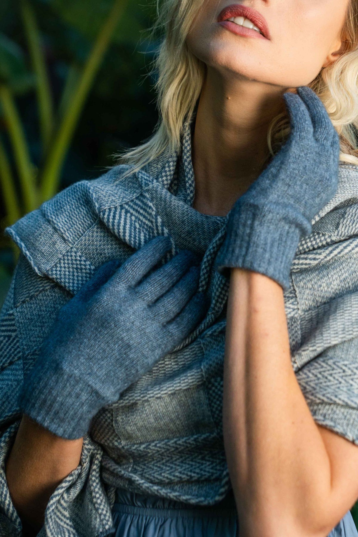 A close-up lifestyle shot of a woman wearing the Plain Possum Merino Gloves in Riviera by Koru and a matching blue-gray patterned wrap or shawl.