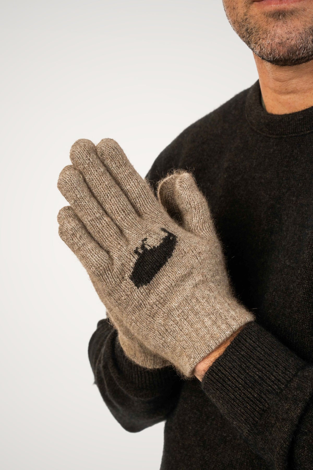 A close-up of a man wearing the Kiwi Possum Merino Gloves in Mocha by Koru, paired with a dark brown sweater against a light gray background.