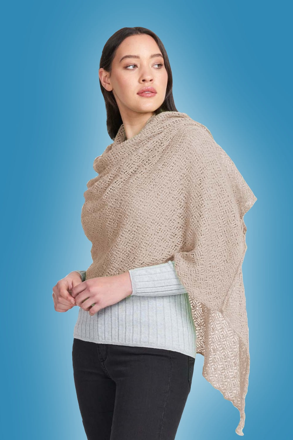 Woman wearing the Alpaca Lace Wrap in Light Camel by Royal Merino against a blue background