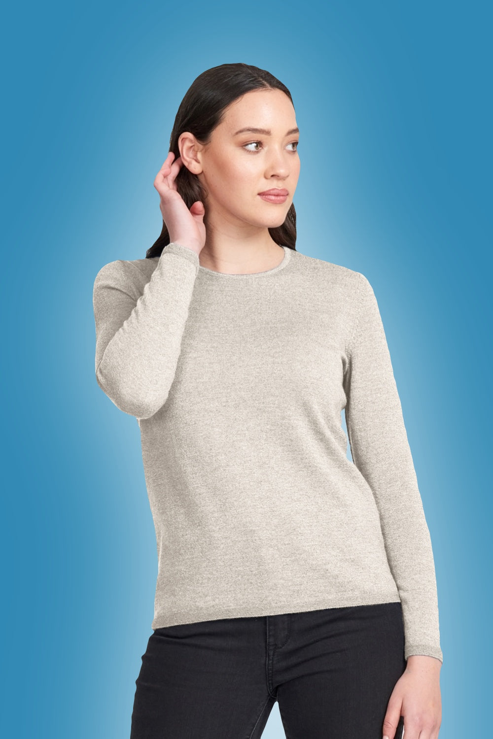 Woman wearing the Classic Merino Crew in Light Sand by Royal Merino against a blue background
