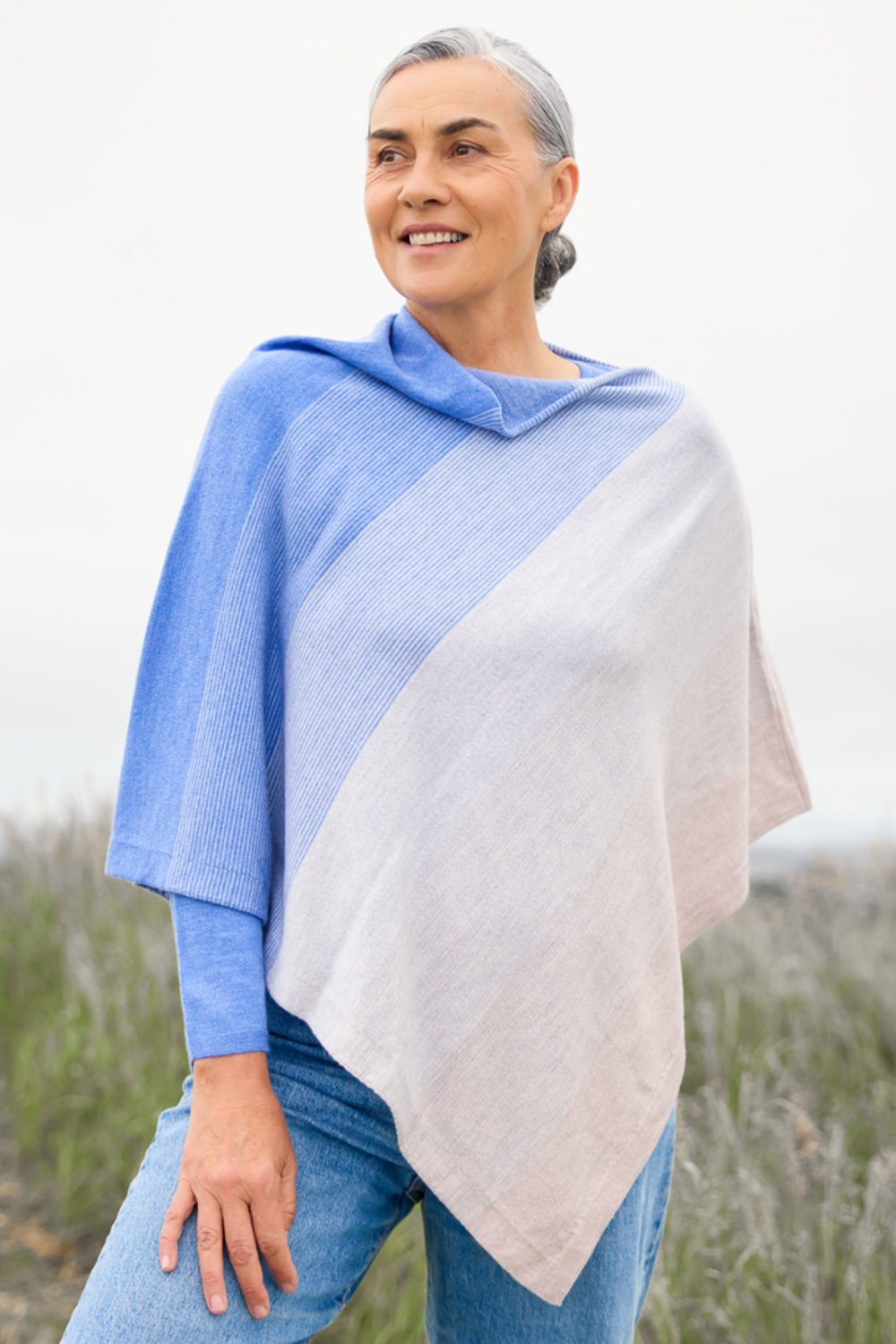 Woman wearing the Graduated Stripe Merino Poncho in Chambray by Royal Merino, standing in a field.