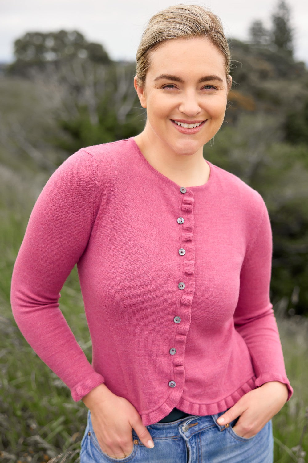 Woman wearing the Frill Trim Merino Cardigan in Azalea by Royal Merino with a blurred natural background