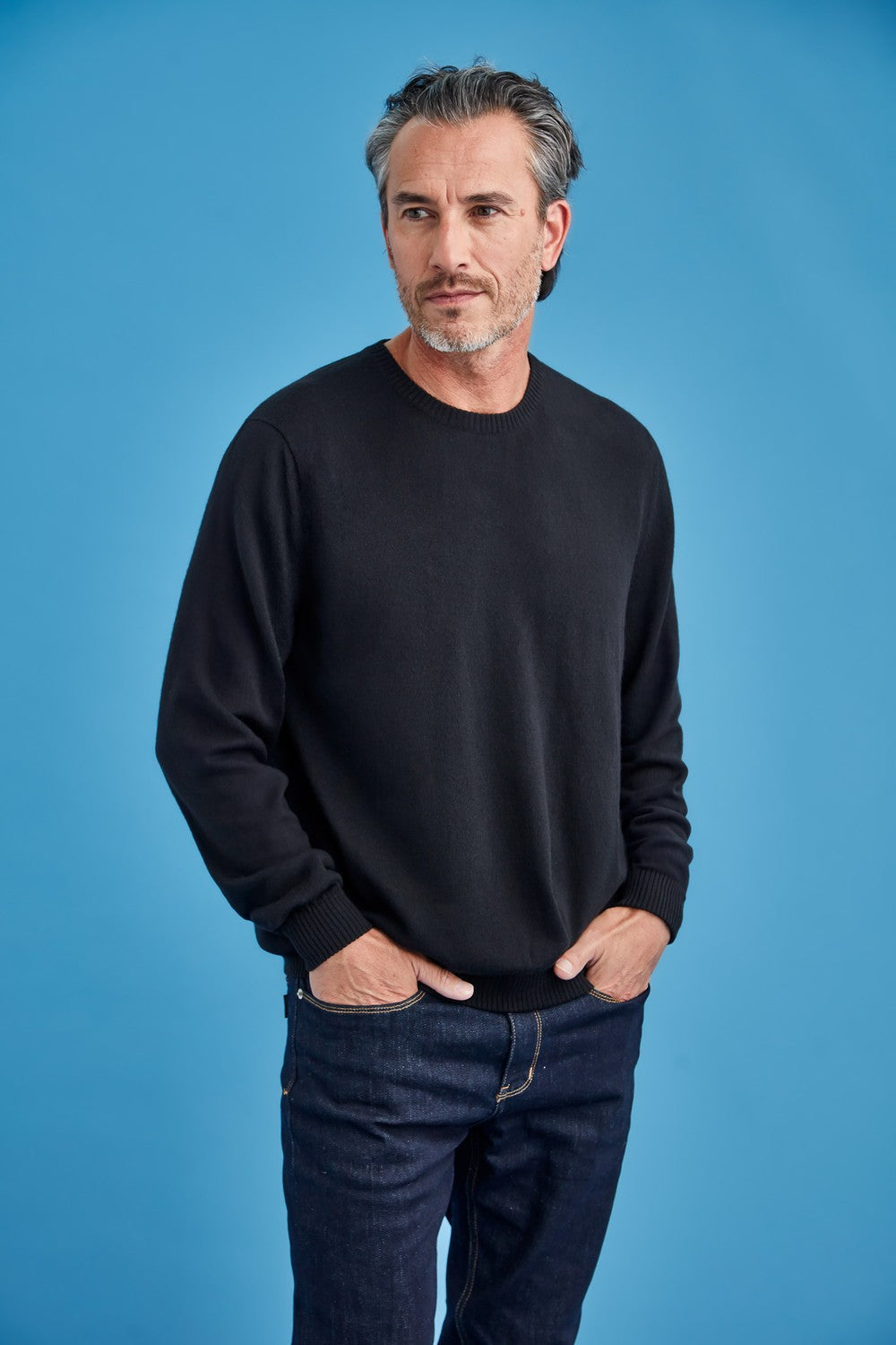 Man wearing the Men's Merino Crew Neck in Black by Royal Merino against a blue background