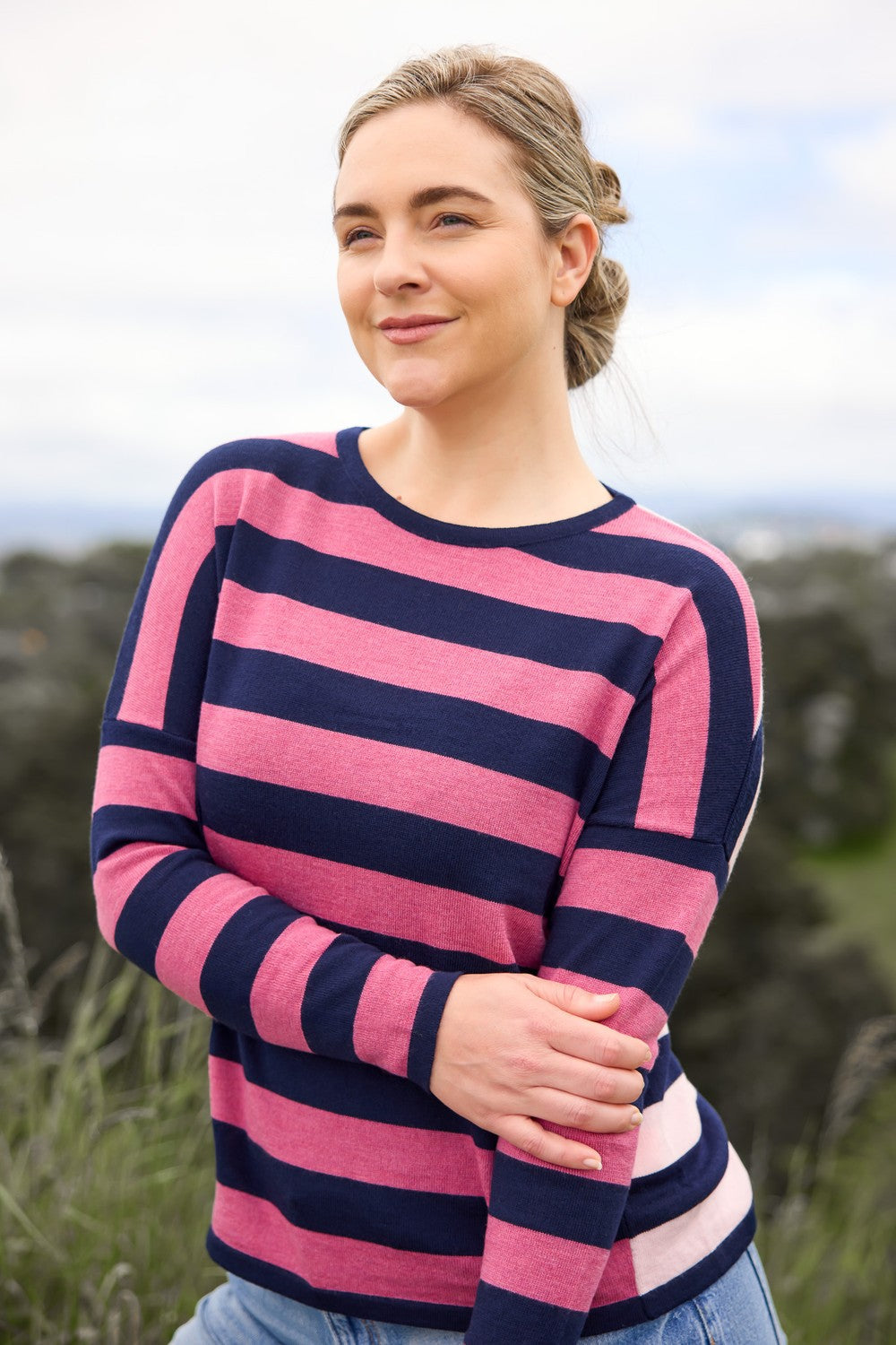 Woman wearing the Striped Drop Shoulder Merino Jumper in Geranium by Royal Merino outdoors with a blurred natural background