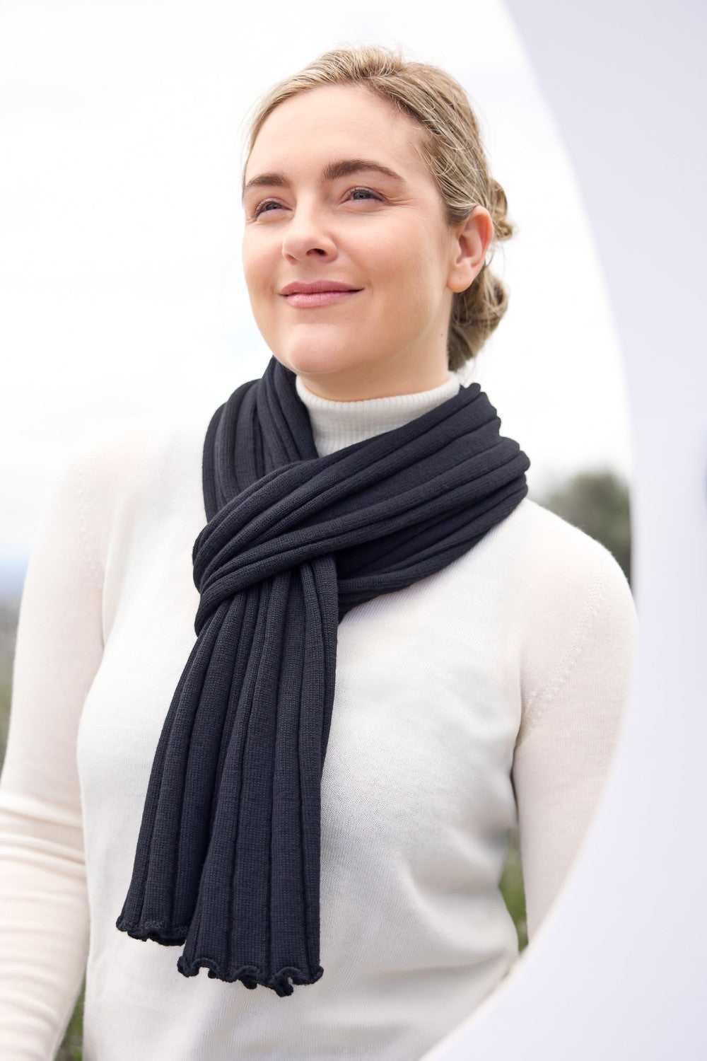 Woman wearing the Rib Merino Scarf in Black by Royal Merino against a white background