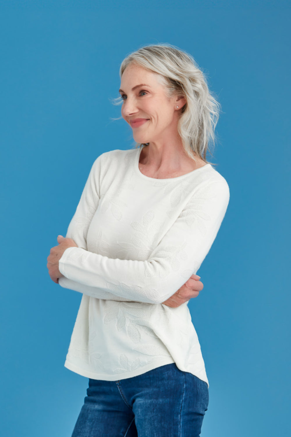 Woman wearing the Woman wearing the Flora Stitch Merino Sweater in Natural by Royal Merino and blue jeans against a blue background