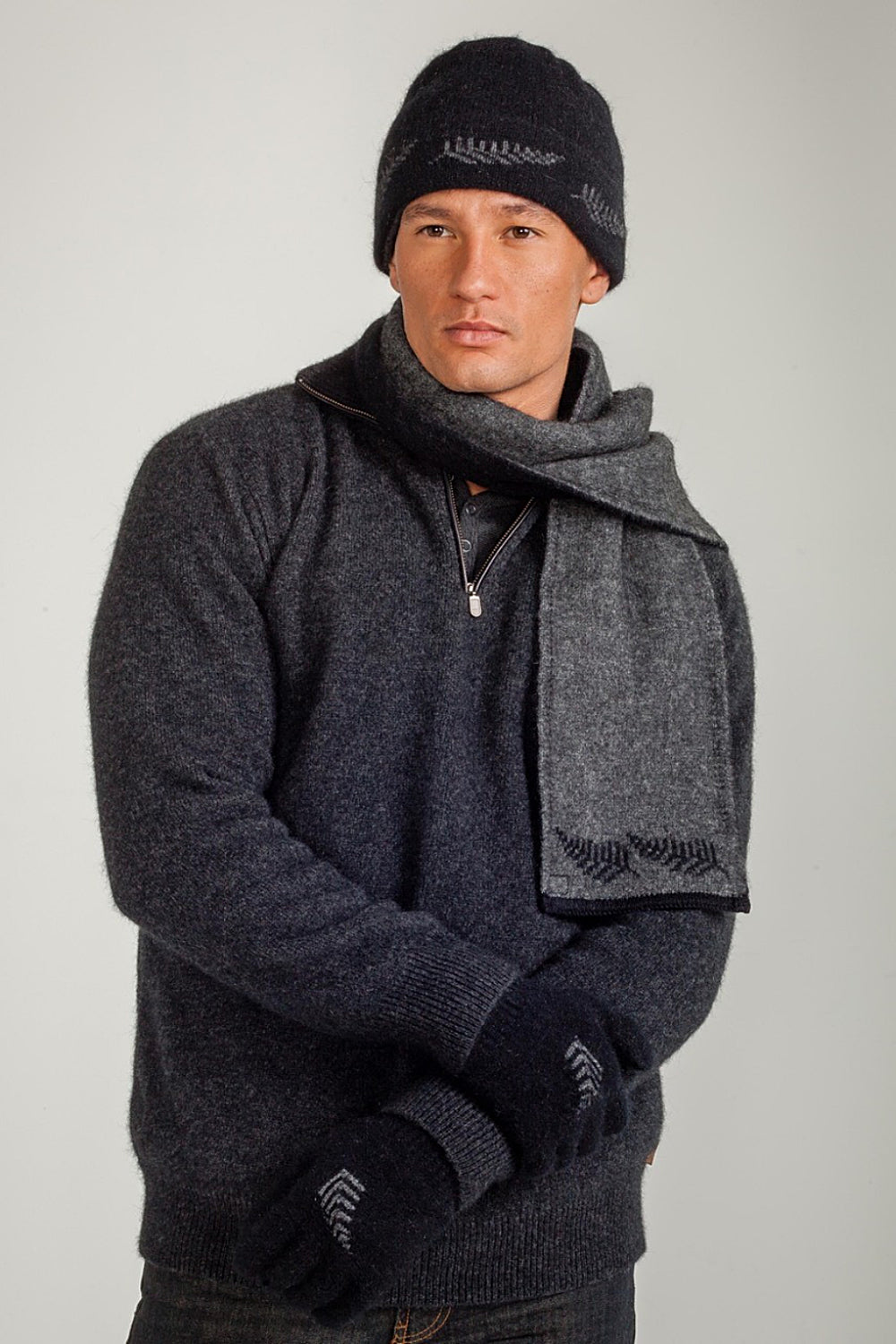 Man wearing a dark gray sweater wearing the Fern Possum Merino scarf, beanie and gloves by Koru, on a light gray background