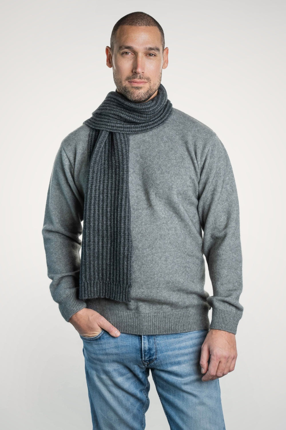 Man wearing a gray sweater and blue jeans with the Ribbed Possum Merino Scarf in Grey by Koru on a white background