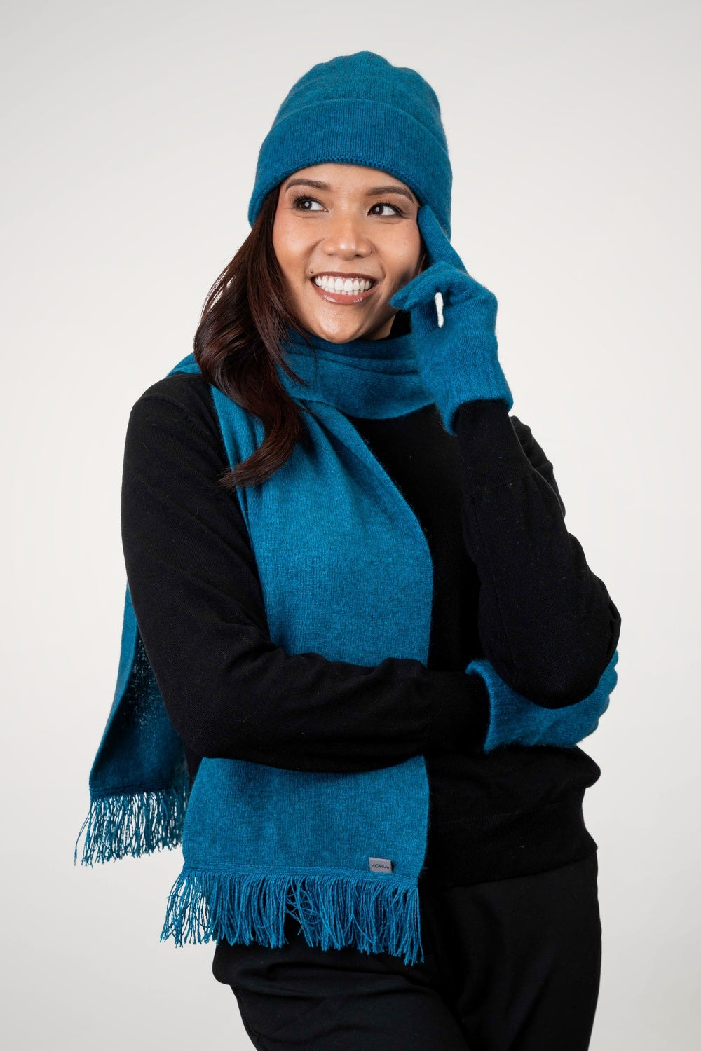 Woman wearing the Fringed Possum Merino Scarf in Pacific by Koru, with matching hat and gloves on a white background