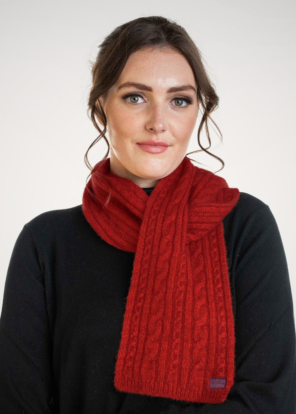 Woman wearing the Cable Possum Merino Scarf in Rata by Koru against a white background