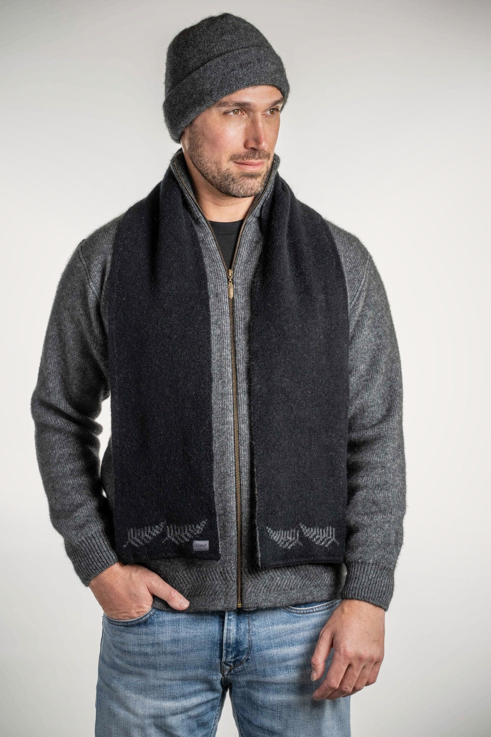 Man wearing a gray sweater with the Fern Possum Merino Scarf in Black/Grey by Koru against a white background
