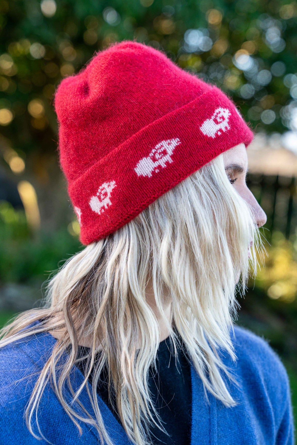 A woman shown in side profile wearing the Sheep Possum Merino Beanie in Rata by Koru, photographed outdoors with blurred greenery in the background.