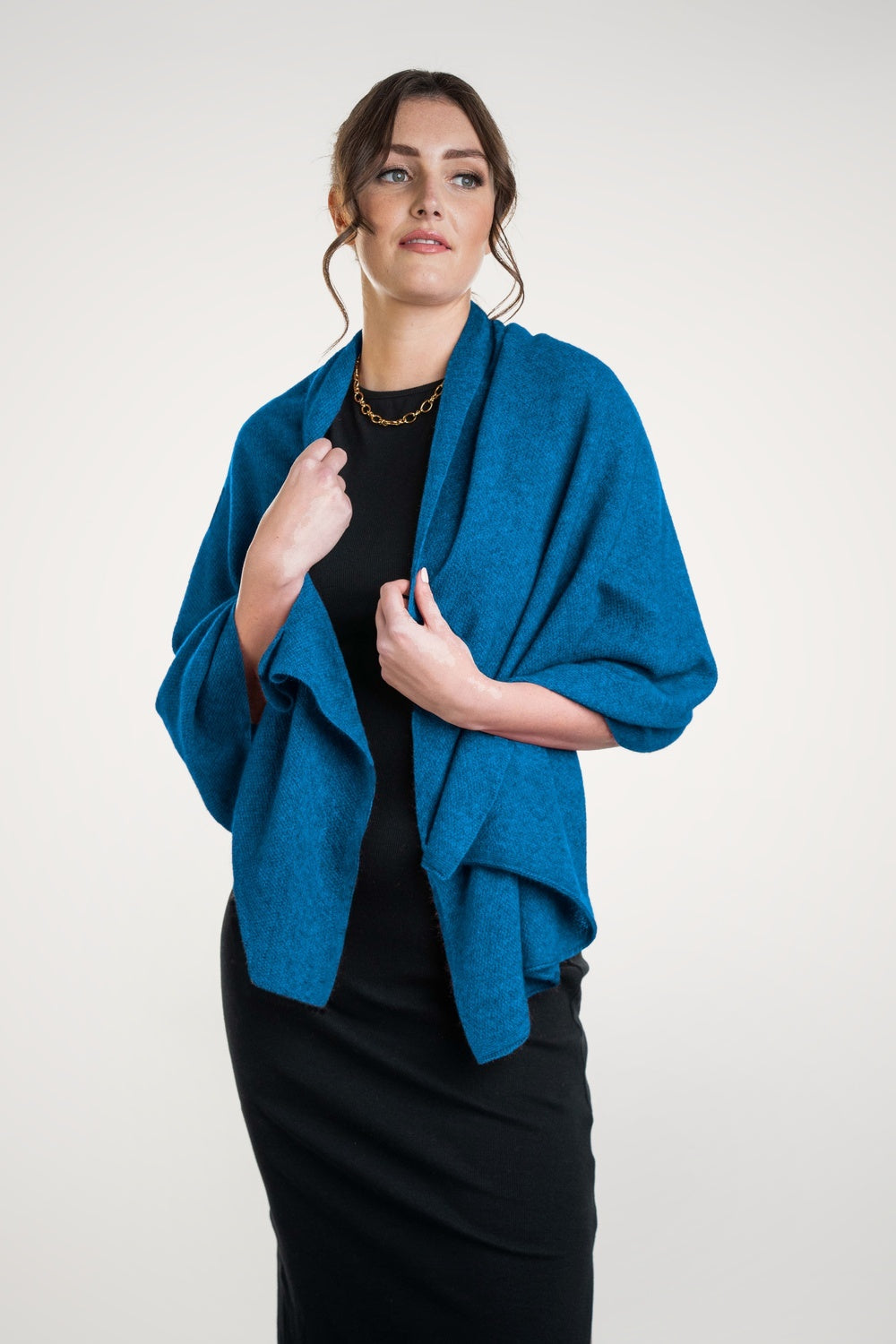 Woman wearing the Moss Stitch Possum Merino Wrap in Pacific by Koru over a black outfit on a white background