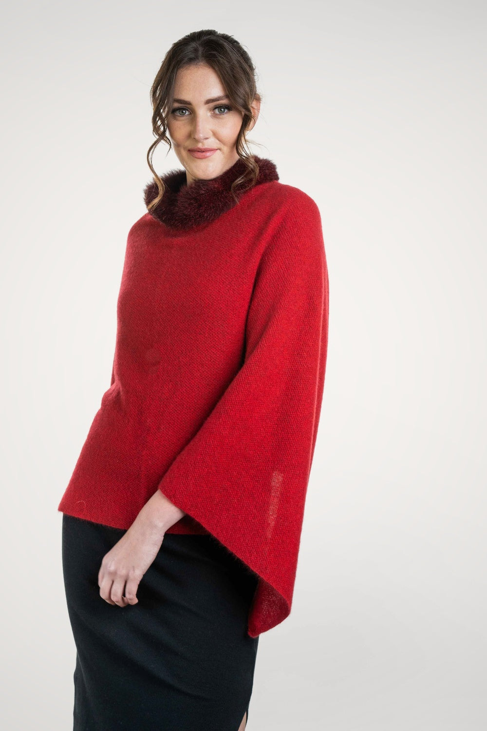Woman wearing the Fur Trim Possum Merino Poncho in Rata/Rossi by Koru with a white background
