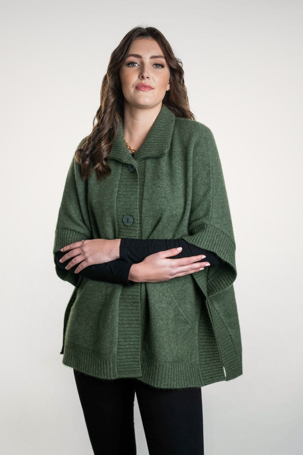 Woman wearing the Possum Merino Cape with Pockets in Moss by Koru against a white background