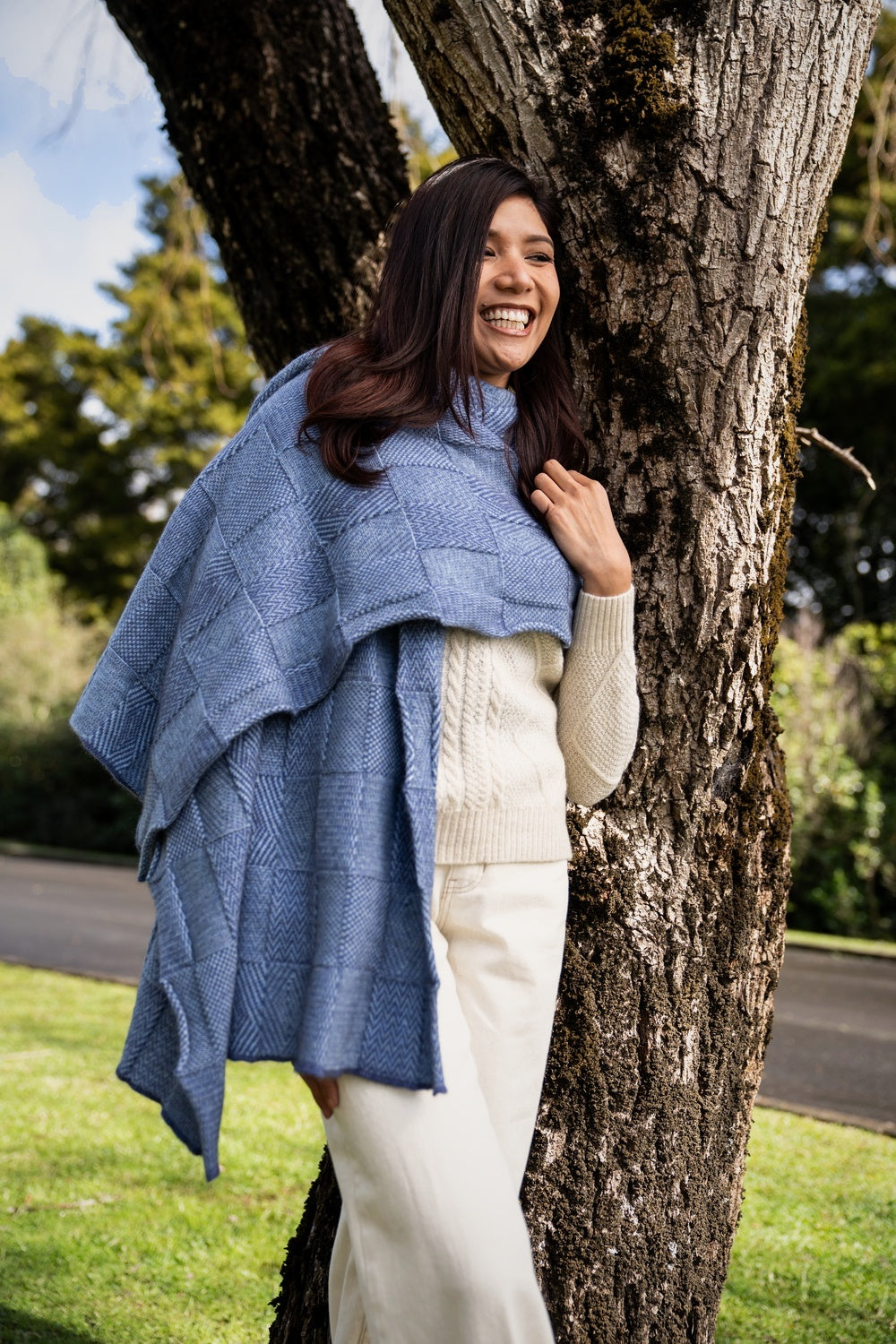 Woman wearing the Jacquard Possum Merino Wrap in Sky/Periwinkle by Koru standing next to a tree outdoors