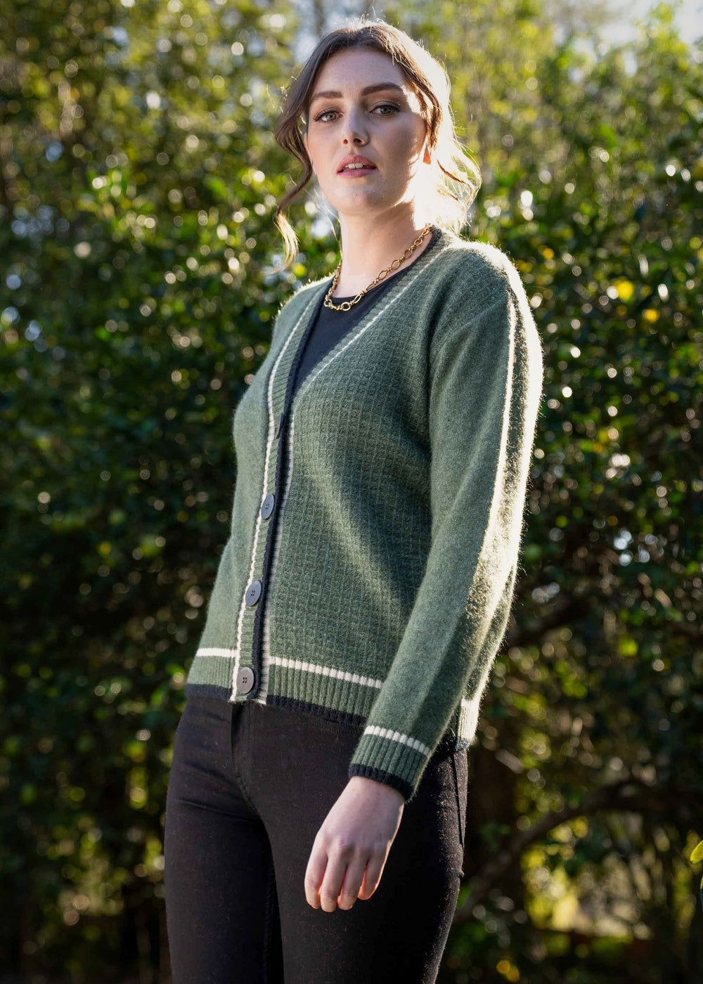 Woman wearing the Contrast Textured Possum Merino Cardigan in Moss by Koru standing outdoors with trees in the background