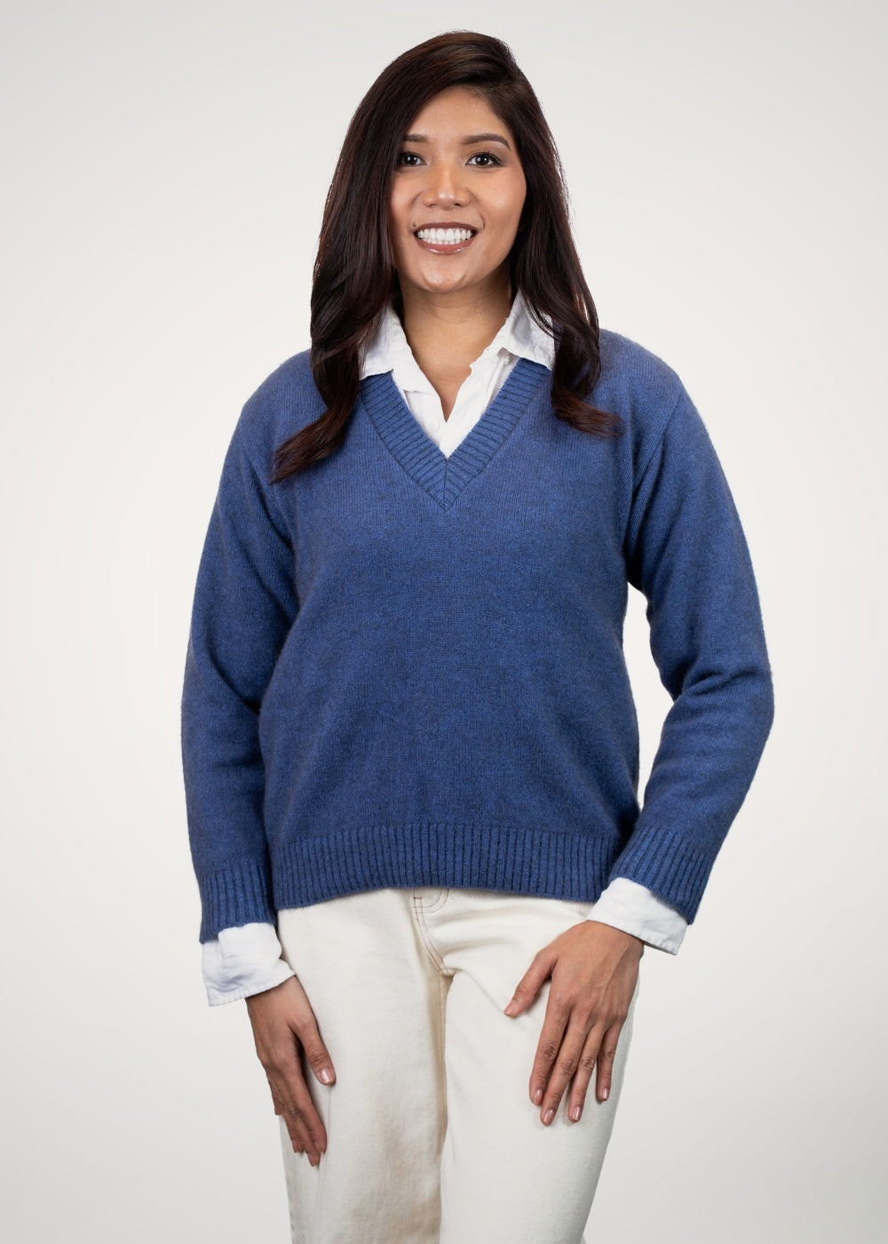 Woman wearing the V Neck Possum Merino Jumper in Periwinkle by Koru over a white shirt with beige pants on a white background