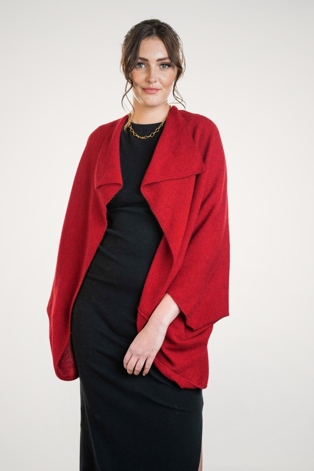 Woman wearing the Moss Stitch Possum Merino Shrug in Rata by Koru over a black dress on a white background