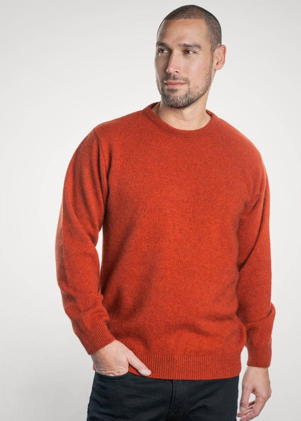 Man wearing the Crew Neck Possum Merino Jumper in Sienna by Koru with black jeans against a white background, with one hand in his pocket looking off to the side