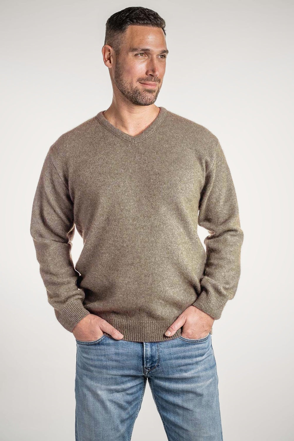 Man wearing the V Neck Possum Merino Jumper in Mocha by Koru, with jeans against a white background
