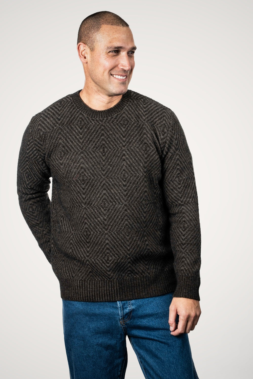 Man wearing the Diamond Plated Crew Possum Merino in Espresso/Suede by Koru and blue jeans against a white background