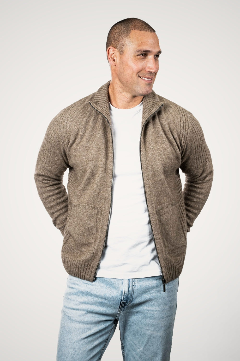 Man wearing the Rib Detail Possum Merino Jacket in Moss by Koru with blue jeans against a white background, unzpped
