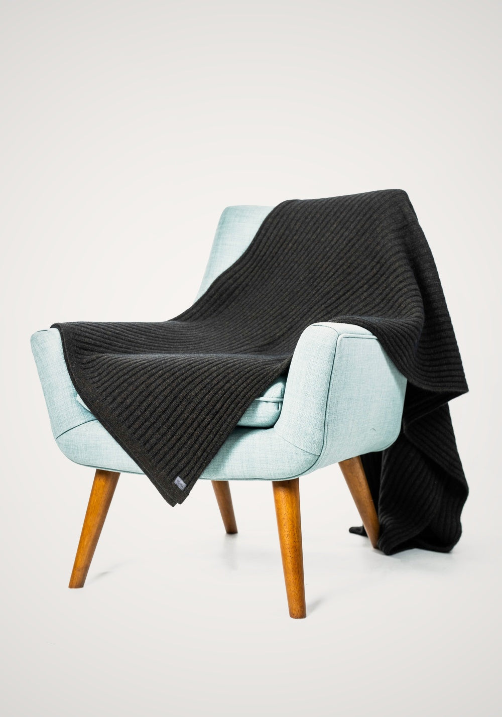 Ribbed Possum Merino Throw in Espresso by Koru draped over a light blue armchair on a white background