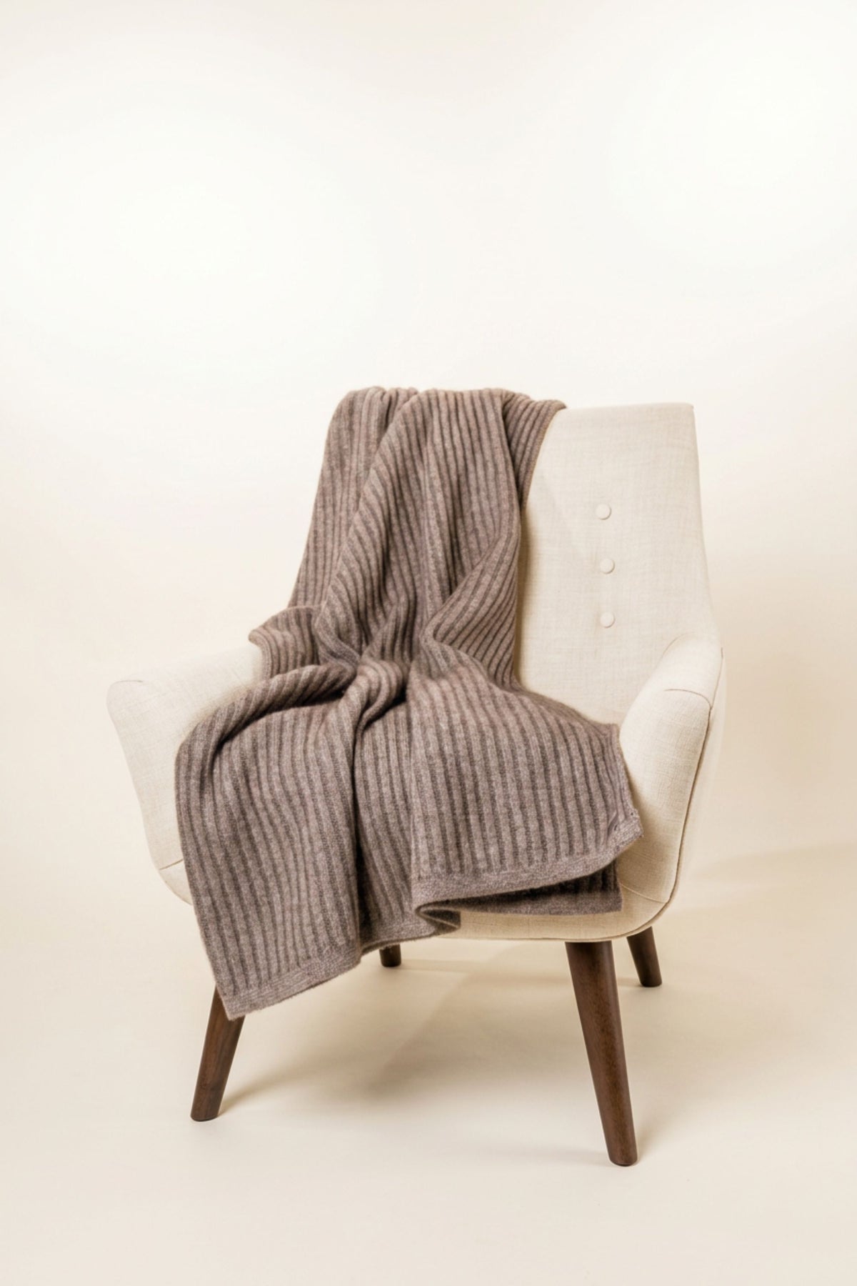 Ribbed Possum Merino Throw in Mocha by Koru draped over a cream armchair on a white background