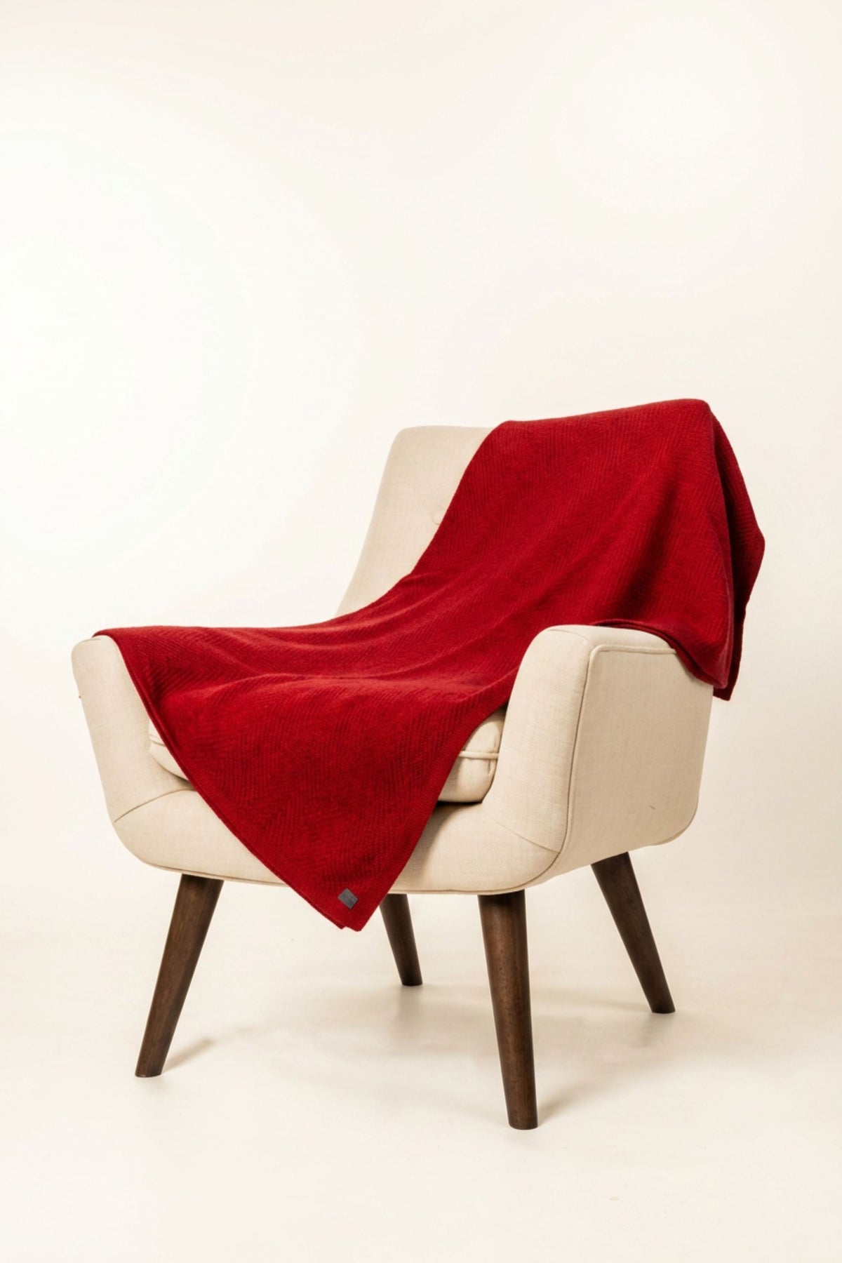 Cream chair with the Plated Herringbone Possum Merino Throw in Rata/Red by Koru draped over it on a white background