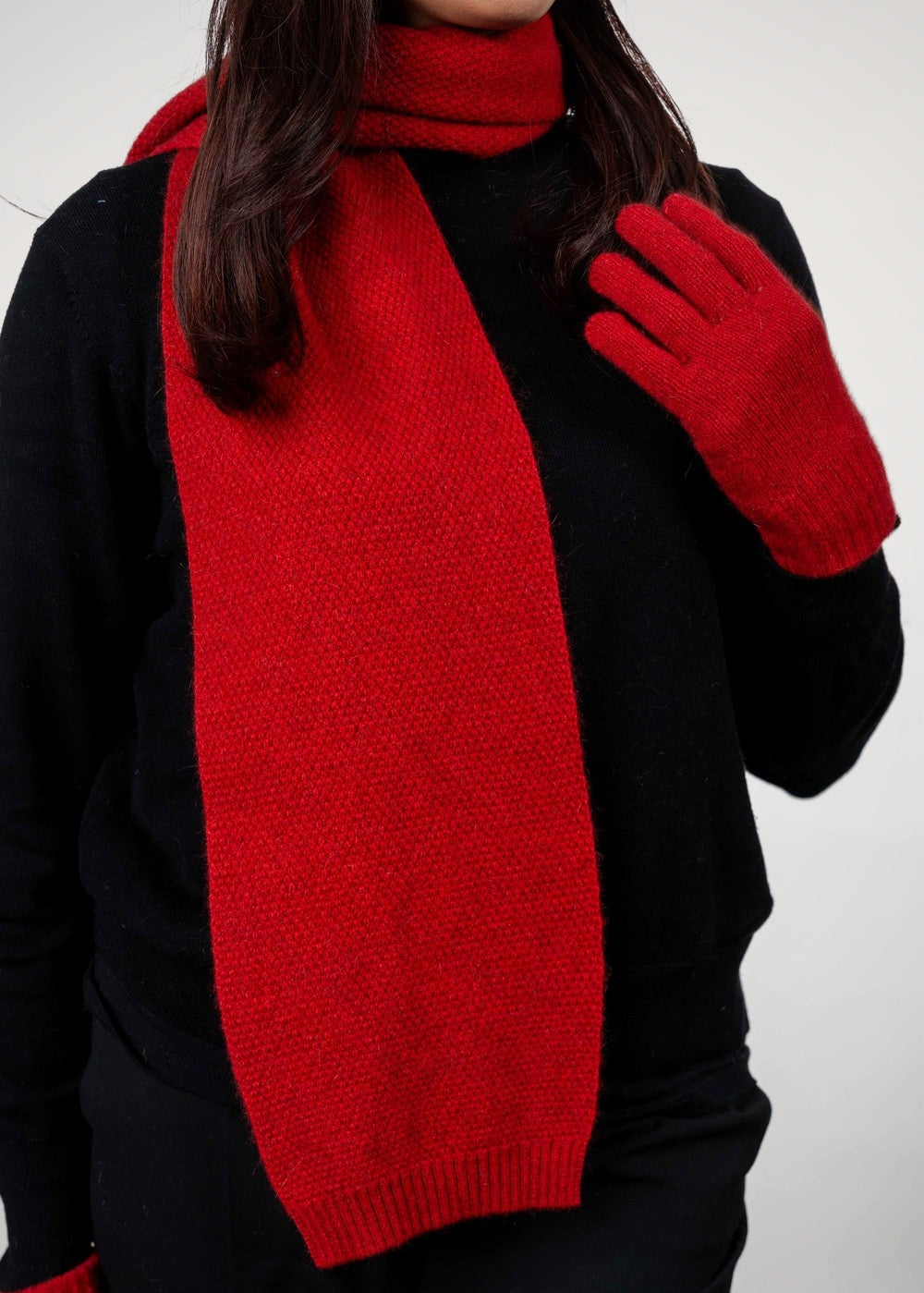 Person wearing the Moss Stitch Possum Merino Scarf in Scarlet by Trilogy and matching gloves on a white background