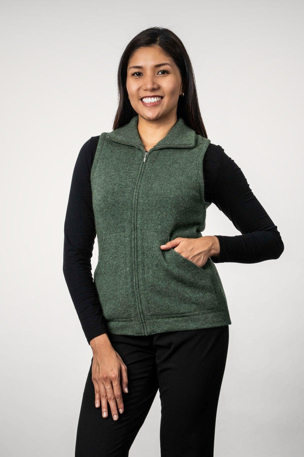Woman wearing the Zip Possum Merino Vest in Fern by Trilogy over a black long-sleeve shirt on a white background