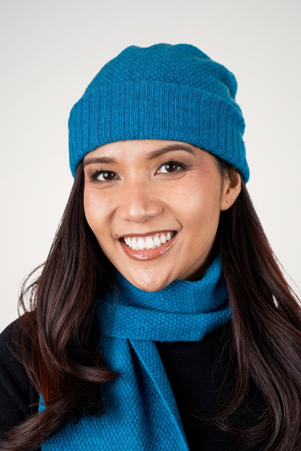 Woman wearing the Moss Stitch Possum Merino Beanie in Teal by Trilogy and matching scarf against a white background