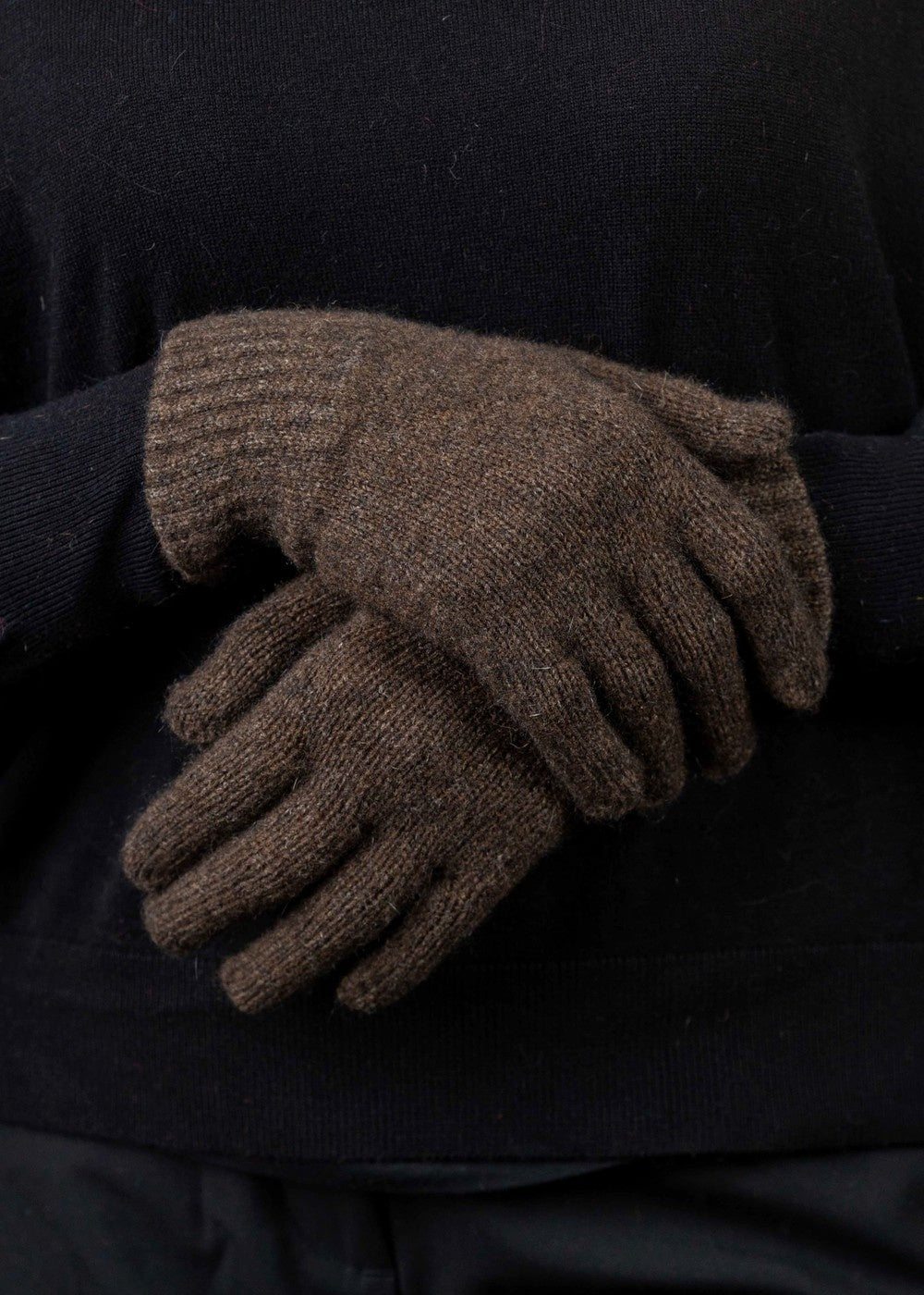 Plain Possum Merino Gloves in Cocoa by Trilogy worn by a person wearing a dark sweater against a black background