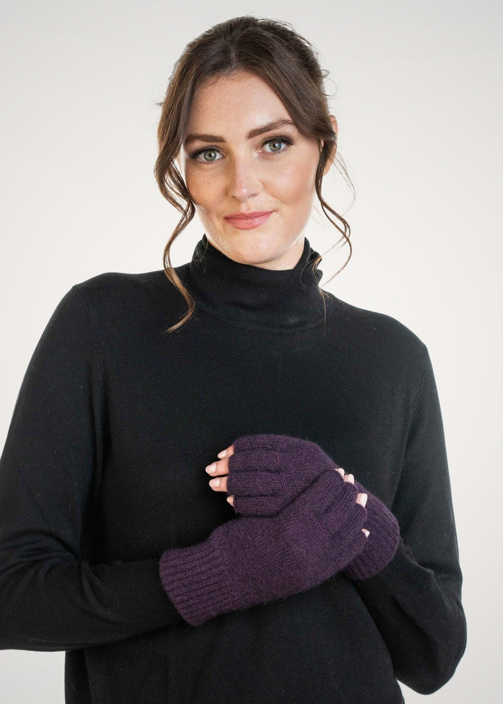 Woman wearing a black turtleneck sweater and Fingerless Possum Merino Gloves in Aubergine by Trilogy against a white background