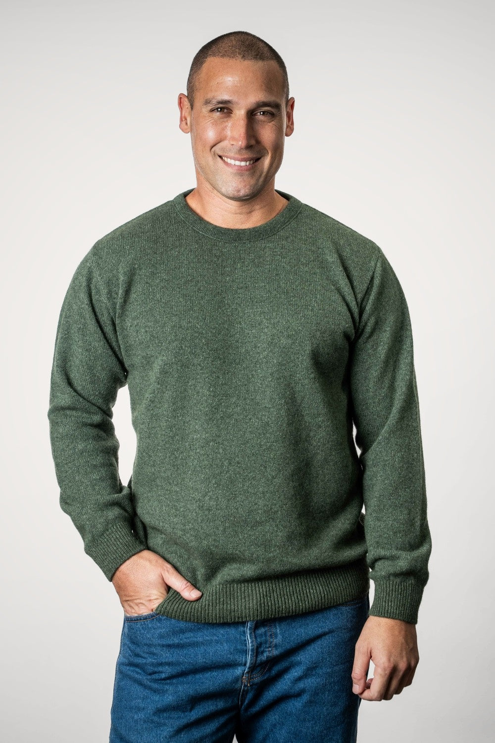 Man wearing the Classic Possum Merino Crew Neck in Fern by Trilogy and blue jeans against a white background